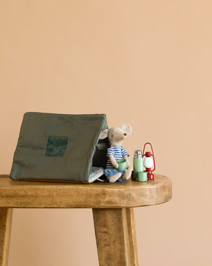 The Maileg LouiMax Little Explorer Set features a toy mouse in a striped shirt with a single tent, miniature lantern, and thermos on a wooden table—perfect for displaying Maileg mouse accessories against a plain beige background.