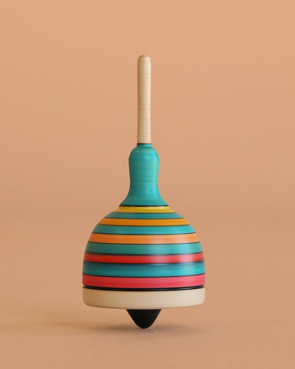 The Mader Fridolin Spinning Top - Blue and Yellow, featuring a colorful domed fingertop with horizontal stripes, spins upright on a smooth, peach-colored surface and background.