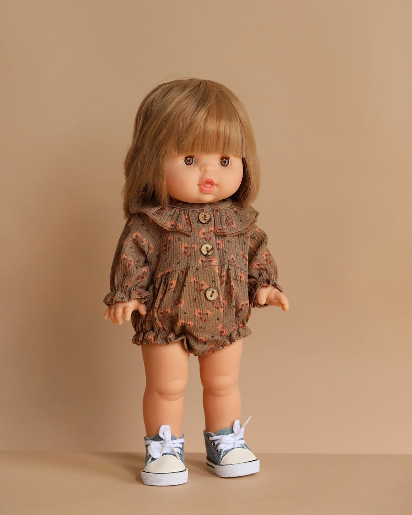 The Minikane Standing Doll (14") - Zoelie, featuring straight blonde hair with bangs, wears a brown collared romper with orange patterns and gray sneakers with white laces, standing against a beige background.