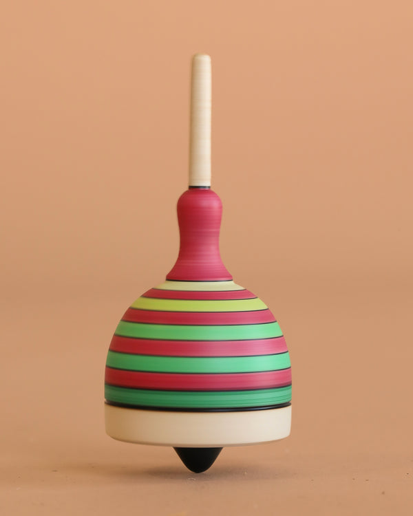 The Mader Fridolin Spinning Top - Green and Red features bold stripes and stands upright on a smooth surface against a plain peach background.