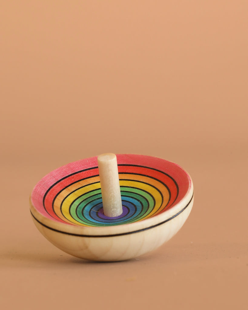 The Mader UFO Spinning Top - Red Rainbow features vibrant rainbow rings on maple wood, displayed against a plain beige background.