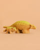 The Bumbu Handmade Wooden Ankylosaurus Dinosaur Set features two handcrafted figurines, large and small, with yellow bodies and green backs on a peach background—ideal as an educational toy for curious minds.