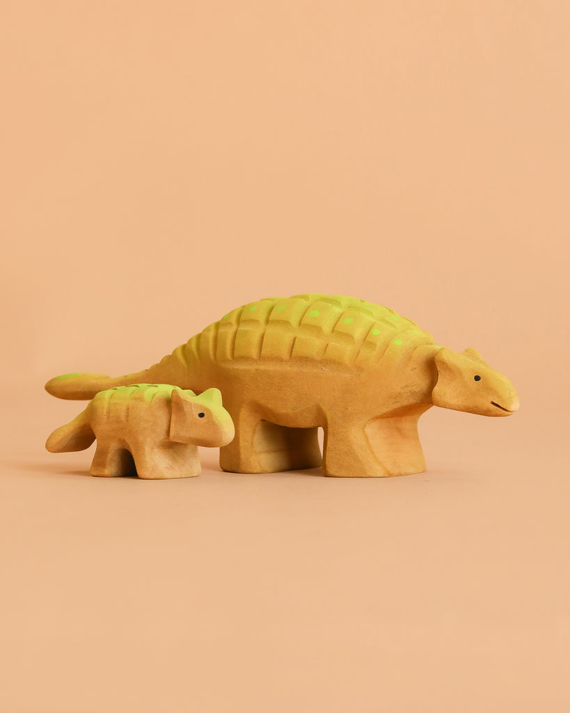 The Bumbu Handmade Wooden Ankylosaurus Dinosaur Set features two handcrafted figurines, large and small, with yellow bodies and green backs on a peach background—ideal as an educational toy for curious minds.