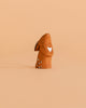 A small, eco-friendly Bumbu Handmade Wooden Curious Rabbit figurine sits on a plain peach-colored background.