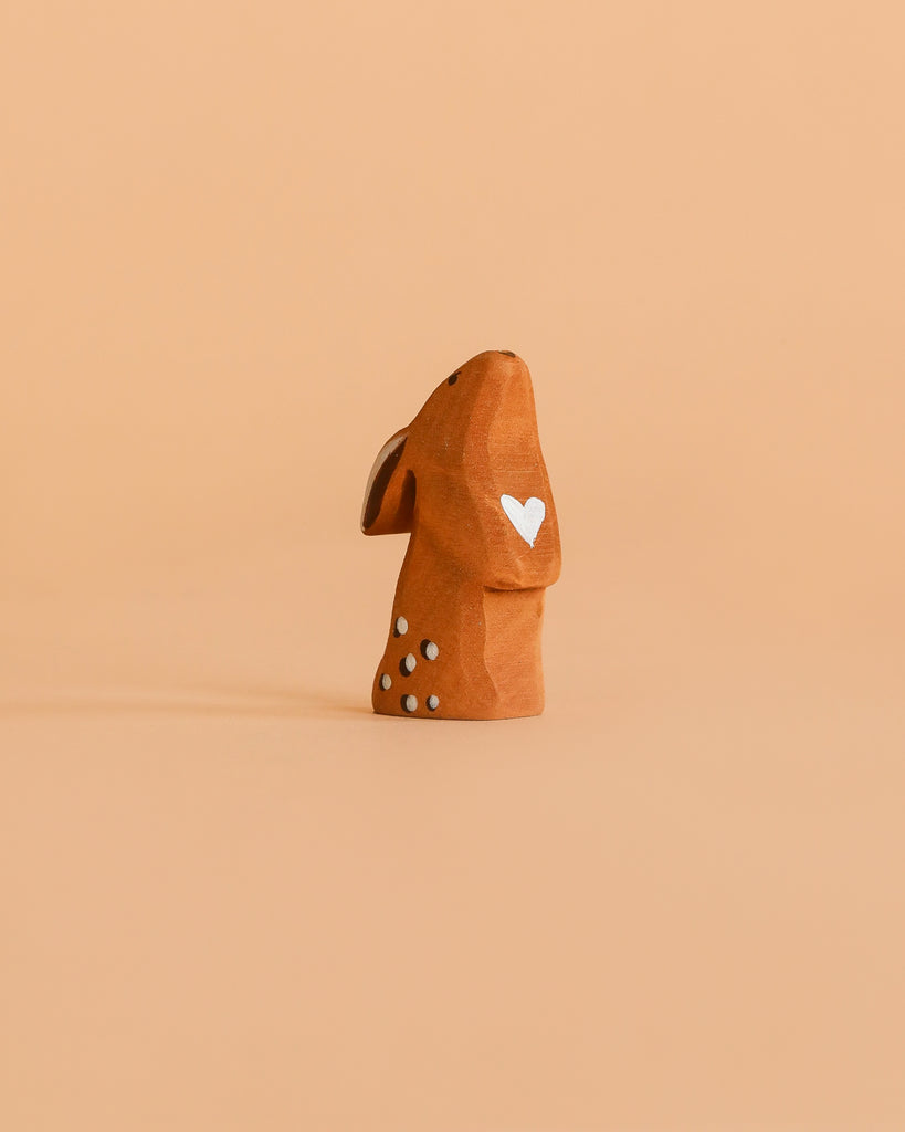 A small, eco-friendly Bumbu Handmade Wooden Curious Rabbit figurine sits on a plain peach-colored background.