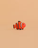 The Bumbu Handmade Wooden Clownfish, featuring orange, white, and black details, is displayed on a peach background. This eco-friendly toy adds minimalistic charm and is ideal for Montessori marine life learning.