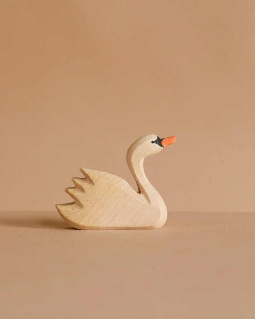 The Ostheimer Handmade Wooden Swan Family Set features small handcrafted wooden swans with orange beaks and simple carved details, displayed on a neutral beige surface against a matching beige background.