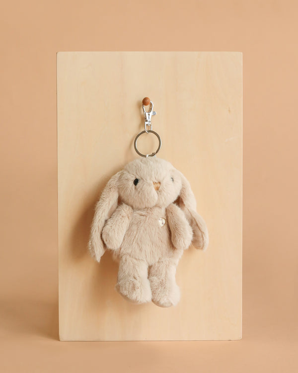 The Snuggle Bunnies - Penelope Keyring in caramel, featuring floppy ears, hangs from a silver clip on a wooden board against a light brown background.