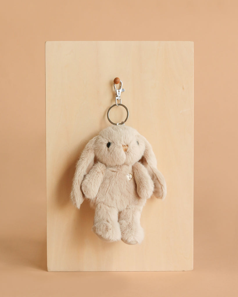 The Snuggle Bunnies - Penelope Keyring in caramel, featuring floppy ears, hangs from a silver clip on a wooden board against a light brown background.