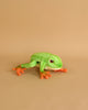A hand-sewn Tree Frog Stuffed Animal, resembling a green frog with orange feet and hands, on a smooth beige background.