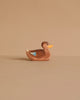 The Ostheimer Duck, Swimming is a small brown wooden figurine with a yellow beak and blue wing marking, handcrafted as a non-toxic toy and shown against a plain beige background.