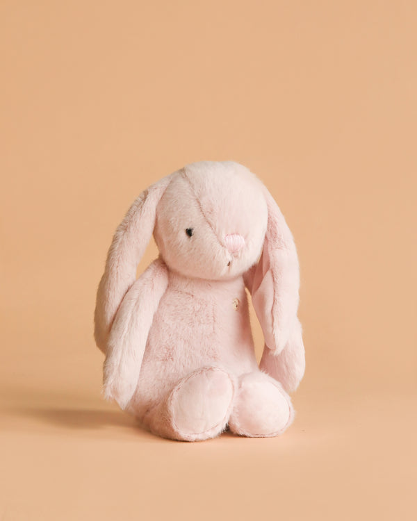 The Snuggle Bunnies - Penelope - Blossom is a soft, light pink stuffed bunny with long floppy ears, sitting upright against a plain peach background—an adorable addition to any plush collection.