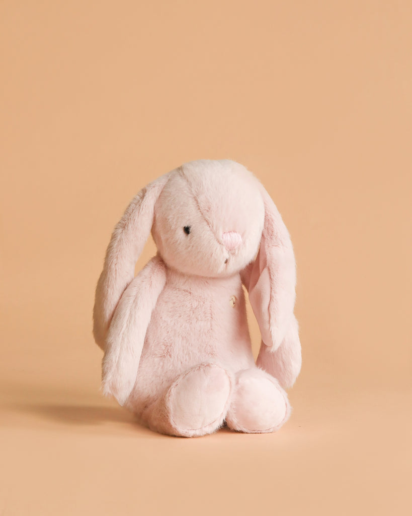 The Snuggle Bunnies - Penelope - Blossom is a soft, light pink stuffed bunny with long floppy ears, sitting upright against a plain peach background—an adorable addition to any plush collection.