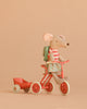 The Maileg Big Sister Tricycle Set features a mouse in a striped shirt, floral skirt, and backpack, riding a red tricycle with a matching wagon against a plain beige background.