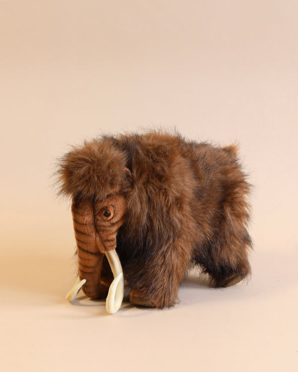 A Mammoth Stuffed Animal featuring long tusks and shaggy brown fur, standing against a plain, light-colored background. This high-quality plush toy captures the essence of the prehistoric creature with exceptional quality.