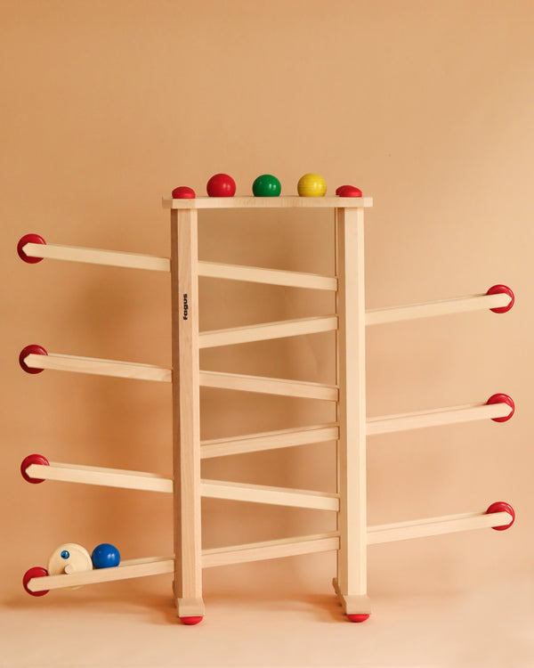 A Fagus XL Ball Run toy rack with colorful balls on a beige background. The rack has multiple levels, each with hooks holding balls in red, green, blue, and yellow.