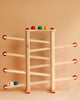 A Fagus XL Ball Run toy rack with colorful balls on a beige background. The rack has multiple levels, each with hooks holding balls in red, green, blue, and yellow.