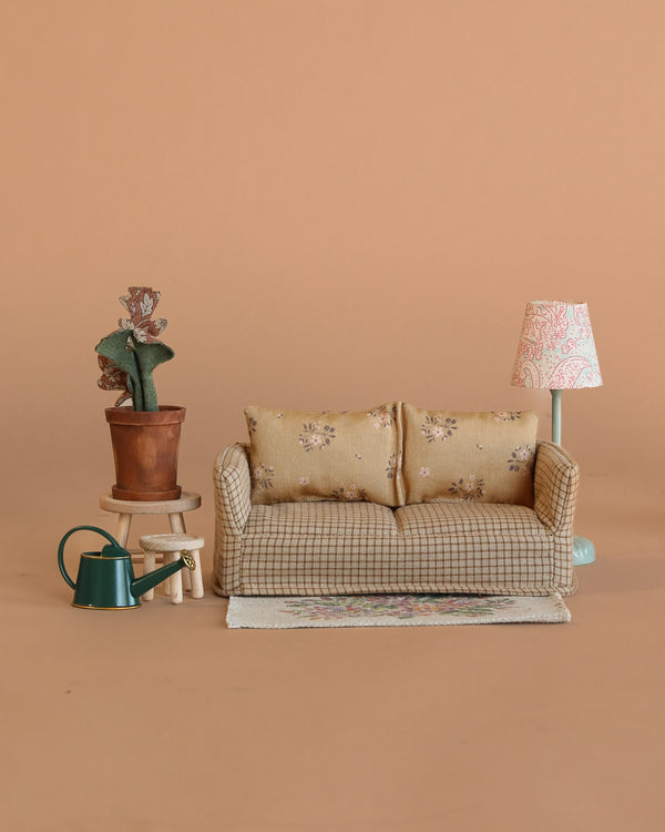 A Maileg Living Room Set features a miniature couch, patterned rug, potted cactus on a stool, green watering can, and vintage floor lamp—all arranged against a plain beige background.