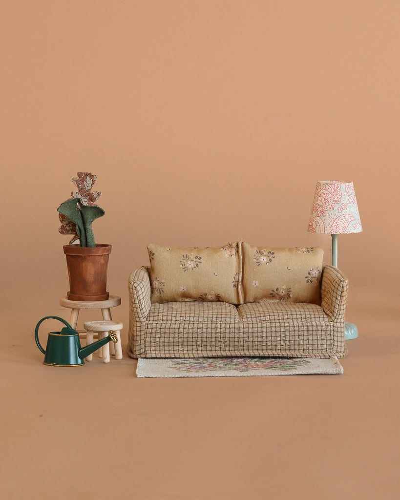 A Maileg Living Room Set features a miniature couch, patterned rug, potted cactus on a stool, green watering can, and vintage floor lamp—all arranged against a plain beige background.