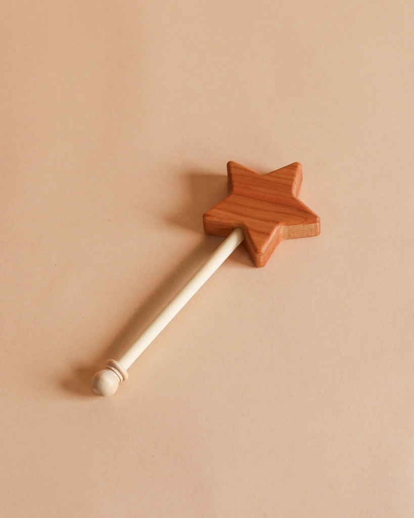 A Bannor Toys Wooden Star Wand with a star-shaped tip and a long handle, laying on a plain pastel beige background.