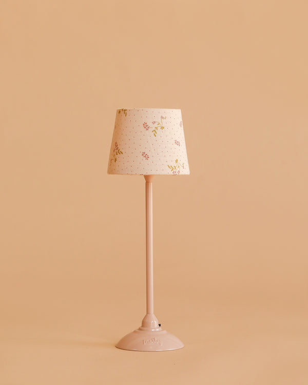 The Maileg Floor Lamp, Miniature - Powder features a pastel pink base and floral-patterned shade, displayed on a matching pink surface with a solid peach background.