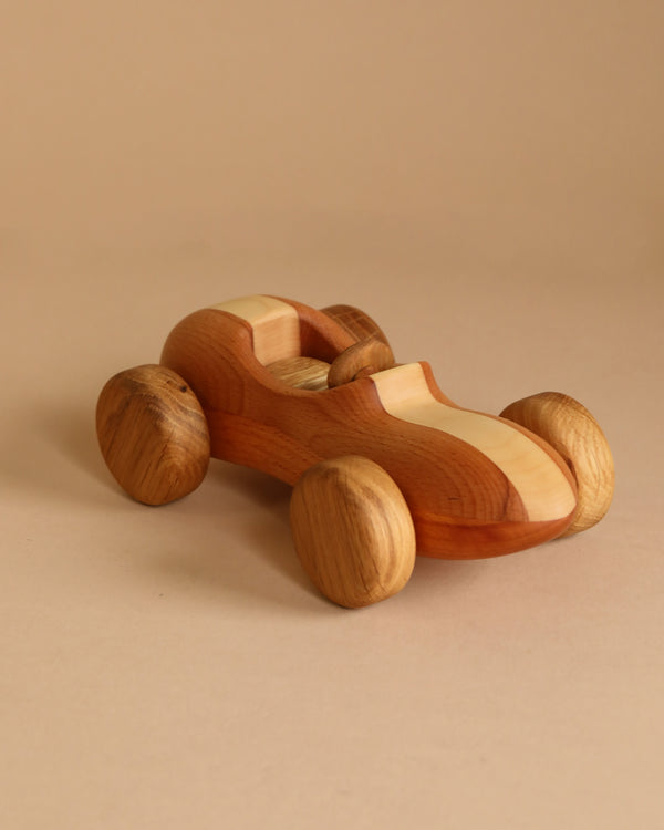 The Handmade Wooden Race Car, crafted from beech wood with a sleek, minimalist design, is displayed on a light brown surface that complements its appearance. Treated with natural linseed oil for an ultra-smooth finish, the car features four wooden wheels and a cut-out cockpit.