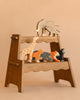 A wooden display shelf features the Holztiger Handmade Wooden Safari Animals Set—handcrafted elephant, giraffe, lion, hippo, tiger, and gorilla—made from maple and beech wood, set against a plain beige background.