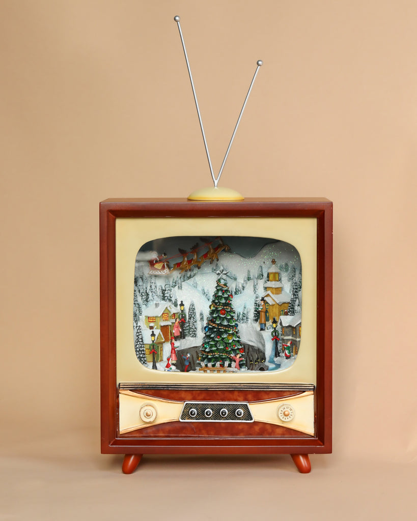 An old-fashioned animated Christmas Music TV With Skaters displaying a detailed winter village scene with a decorated Christmas tree, houses, and figures in festive attire, set against a plain beige background.