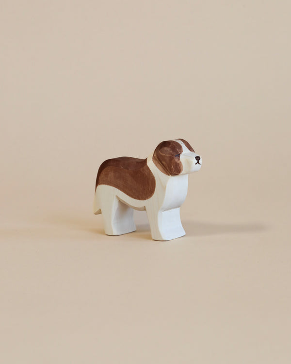 A handcrafted wooden figurine of an Ostheimer Saint Bernhard Dog, painted with brown and white colors, stands against a plain light beige background.
