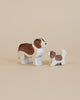 Two handcrafted wooden dog figurines, one larger and one smaller, both painted white with brown patches. They stand facing each other on a plain beige background. The larger figure has a slightly forward-leaning posture, while the smaller one stands straight. Ostheimer Small Saint Bernhard Dog - Head Up is perfect for imaginative play.