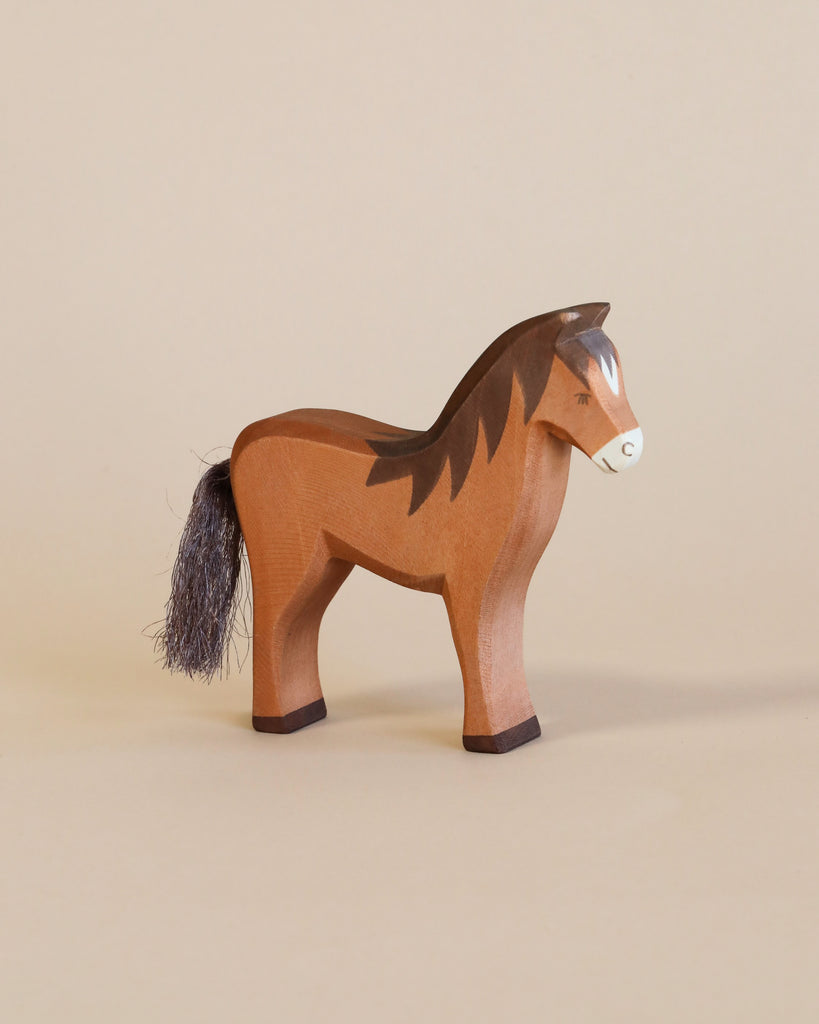 An Ostheimer Handmade Wooden Farm Animals Set toy horse, featuring painted details and a dark brown mane and tail, stands on a light beige surface with a matching background, highlighting the beauty of non-toxic wooden toys.