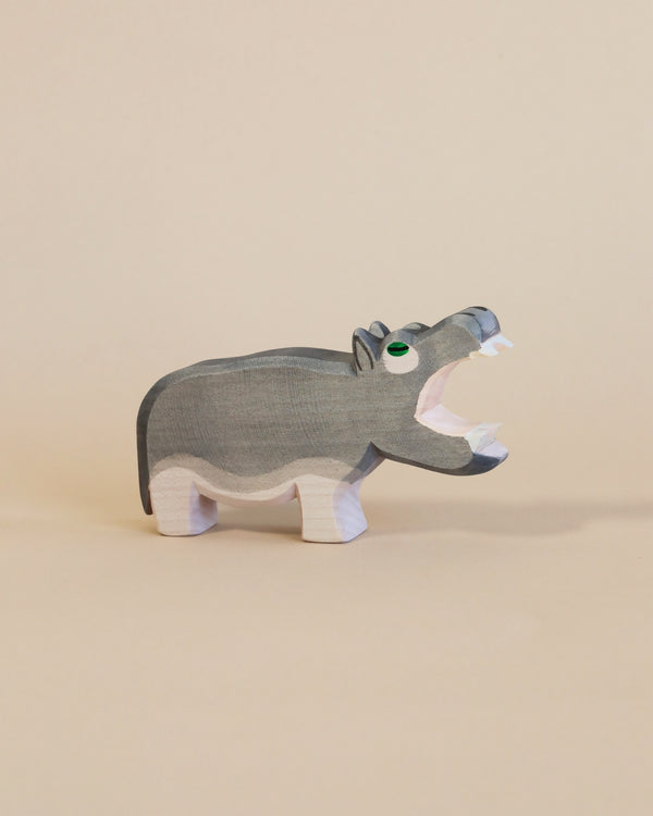 A Ostheimer Hippo - Open Mouth toy, handcrafted from sustainably sourced materials, features a grey body with white details on its paws and mouth, standing against a plain beige background. Its eyes are accentuated.