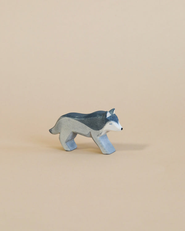 A small, handcrafted Ostheimer Wolf - Running figurine, depicted with a grey and white coat, stands against a soft beige background.