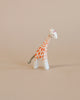 A small Ostheimer Small Giraffe - Head Low stands on a plain light beige background, painted with detailed orange spots and a slight pink detail on the ears.