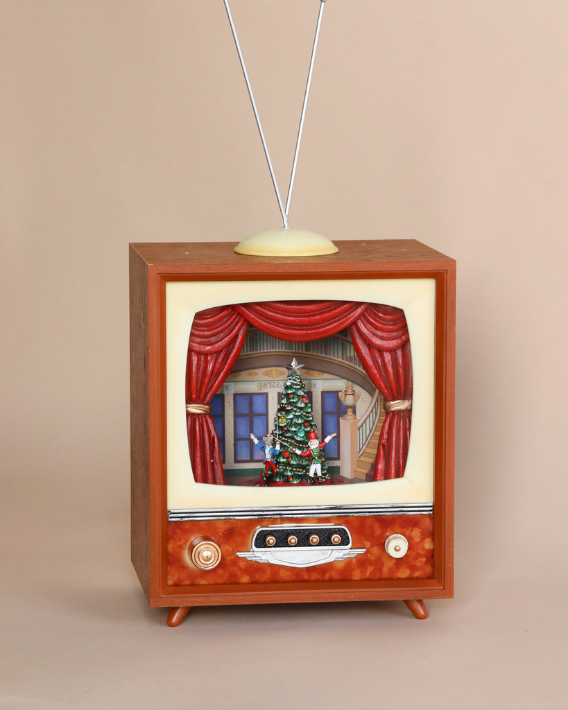 The Christmas Music TV With Nutcracker showcases a festive scene featuring a Christmas tree and decorations on its vintage television with a wooden frame, as soft Christmas melodies play in the background. The beige-set TV is complete with an antenna on top and retro-style dials at the bottom.