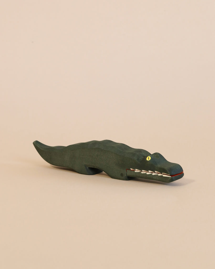 A dark green Ostheimer Crocodile with painted white teeth and yellow eyes, displayed on a plain light beige background.