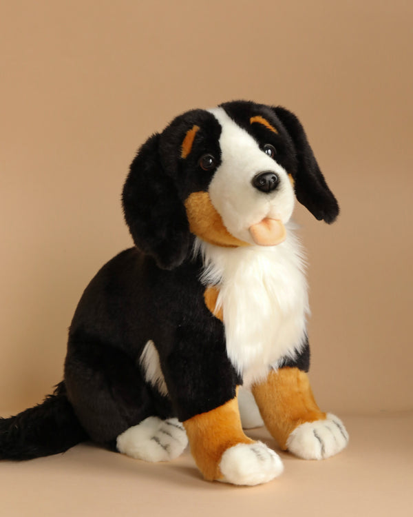 Introducing the Bernese Puppy Dog Stuffed Animal, a delightful plush toy featuring a black, white, and brown coloration. Set against a beige background, this adorable stuffed animal showcases a friendly face with expressive eyes and floppy ears. The toy is meticulously crafted with hand-sewn details, including a white chest that adds to its playful charm.