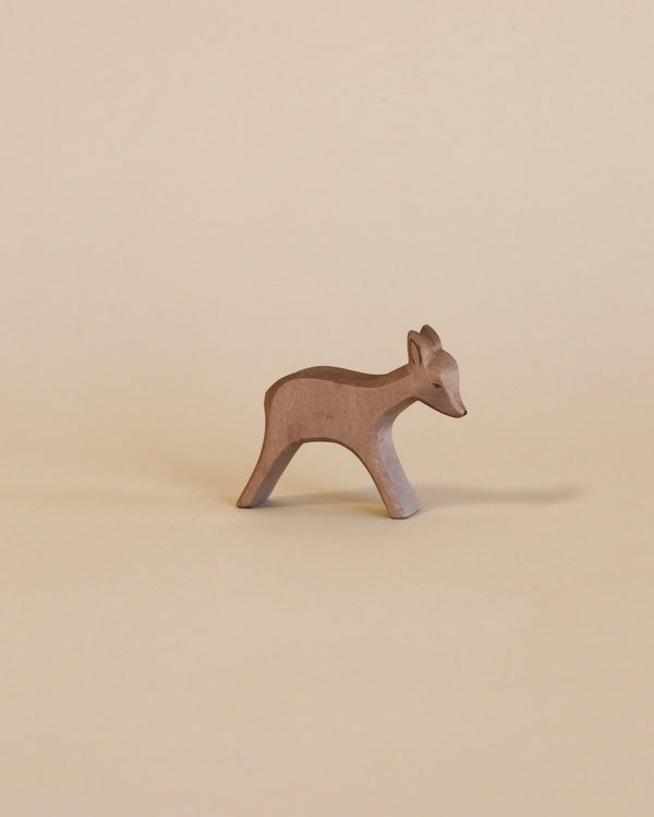 A small, Ostheimer Deer - Standing stands on a plain beige background, showcasing its simple and elegant silhouette with soft curves and pointed ears.