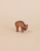 A simple Ostheimer Deer - Eating figurine on a plain beige background. This handcrafted wooden toy has a smooth, curved back and is depicted in a bent grazing pose.