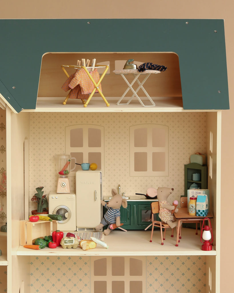The Maileg Fully Furnished Dollhouse Set + Gift With Purchase includes two toy mice, kitchen appliances, groceries, and laundry racks. One mouse stands by the fridge while the other sits at a table with milk and toast. Laundry racks are upstairs.