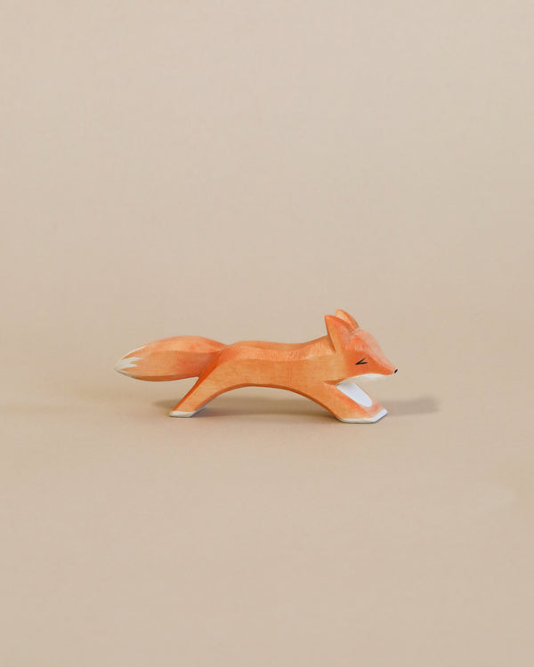 A handcrafted Ostheimer Small Fox - Running figurine, painted orange with white details, depicted in mid-stride against a plain beige background.