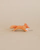 A handcrafted Ostheimer Small Fox - Running figurine, painted orange with white details, depicted in mid-stride against a plain beige background.