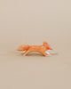 A small, minimalist handcrafted wooden fox figurine from the Ostheimer Handmade Wooden Woodland Animals Set, painted orange with white accents in a running pose—ideal for fans of non-toxic toys and Ostheimer designs.