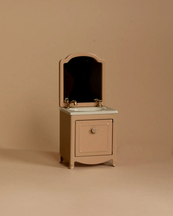 The Maileg Sink Dresser With Mirror, Mouse - Dark Powder is a miniature bathroom vanity with mirror, sink, and gold faucet—ideal for dollhouse bathrooms or as Maileg furniture—shown on a simple beige background.