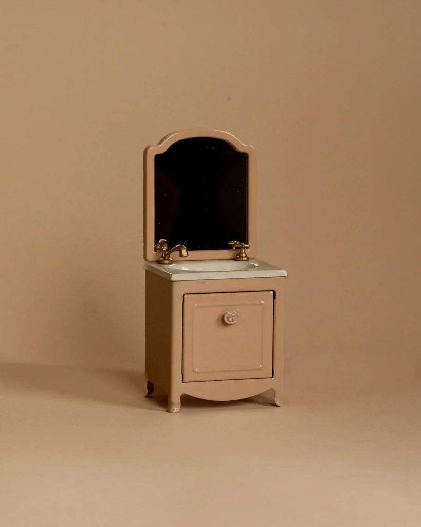The Maileg Little Rabbit’s Bathroom Set features a compact beige vanity cabinet with a mirror, gold faucet, and closed cabinet door, photographed against a solid beige background.