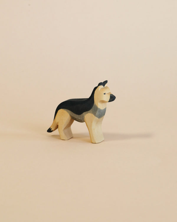 A handcrafted Ostheimer German Shepherd Dog figurine, painted with white and black patches, stands against a soft pink background. The figurine is depicted in a standing pose.