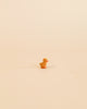 A small, orange Ostheimer Duckling centered on a plain, light beige background. The duck casts a soft shadow behind it, emphasizing its isolated position and evoking the charm of handcrafted wooden toys.