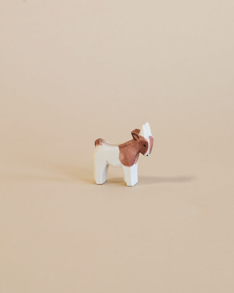 A small donkey from the Ostheimer Handmade Wooden Farm Animals Set, painted white and brown with non-toxic paints, stands on a plain beige background.