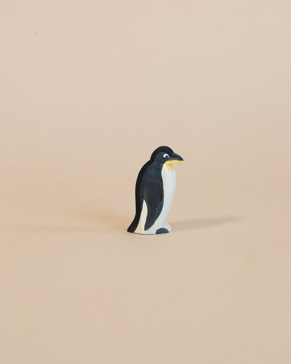 A small Ostheimer Penguin - Head Straight standing upright on a plain, light brown background. The penguin is painted black and white with a yellow beak.