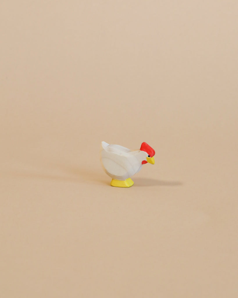 A small, handcrafted Ostheimer White Hen - Standing with a white body, red head, and yellow feet stands isolated against a plain beige background.